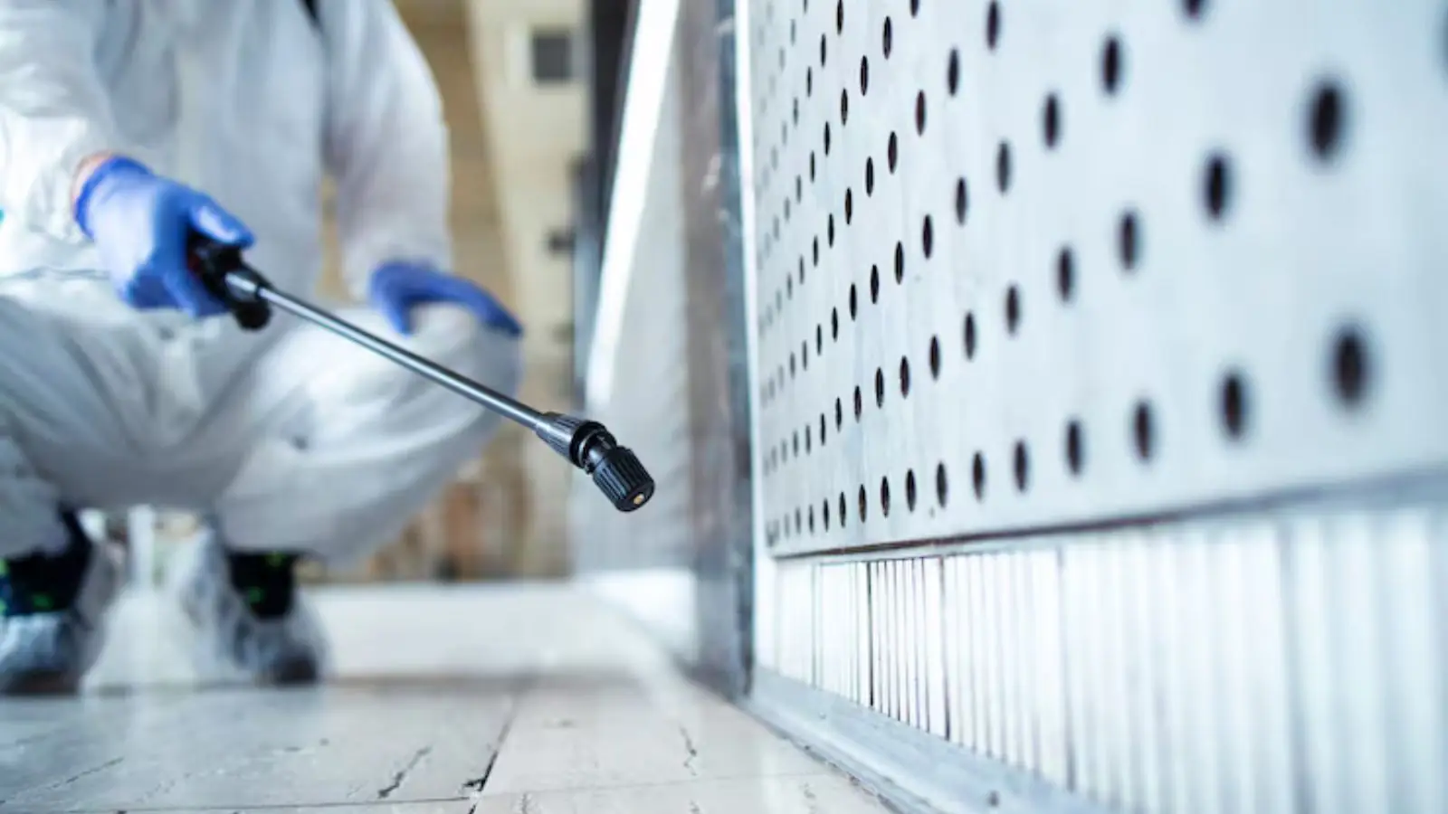 Technician in a protective suit spraying treatment along a commercial wall panel